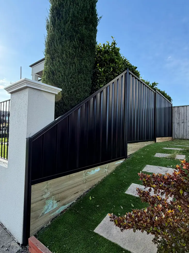 Black Colorbond fence with an angled top panel dropping down to a rendered pillar