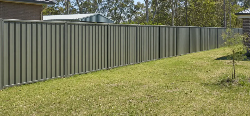 Grey-green Colorbond steel fence along the back boundary of a new house block, with a young tree on the lawn