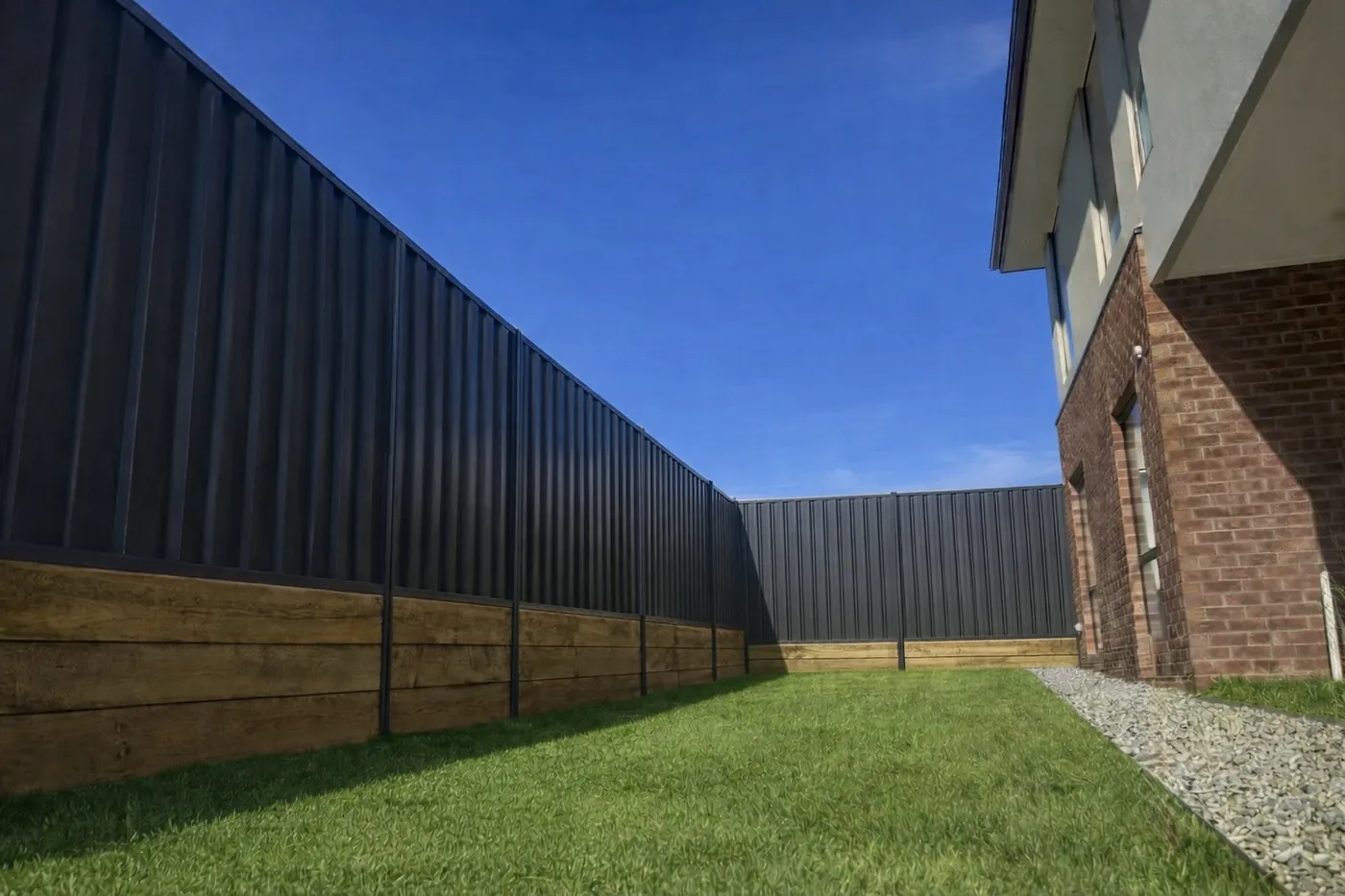 Charcoal Colorbond fence on top of a timber sleeper retaining wall around a backyard lawn