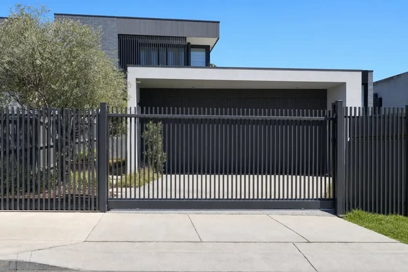 Black steel slat driveway gate closed across the concrete driveway of a modern two-storey Melbourne home