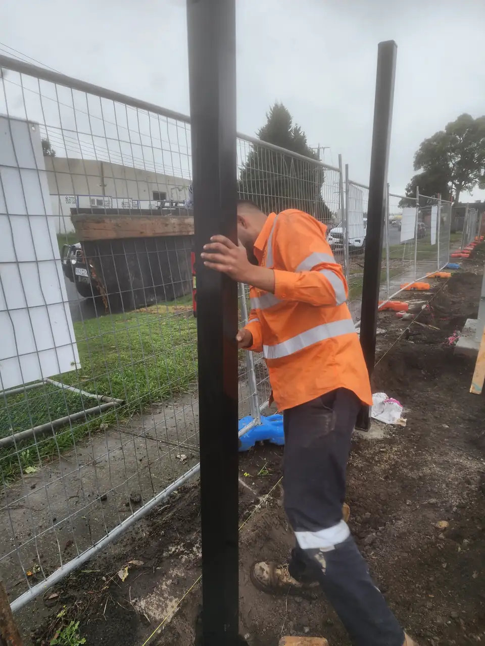 Installer holding a new black steel fence post upright, with a spirit level on it to check it's straight