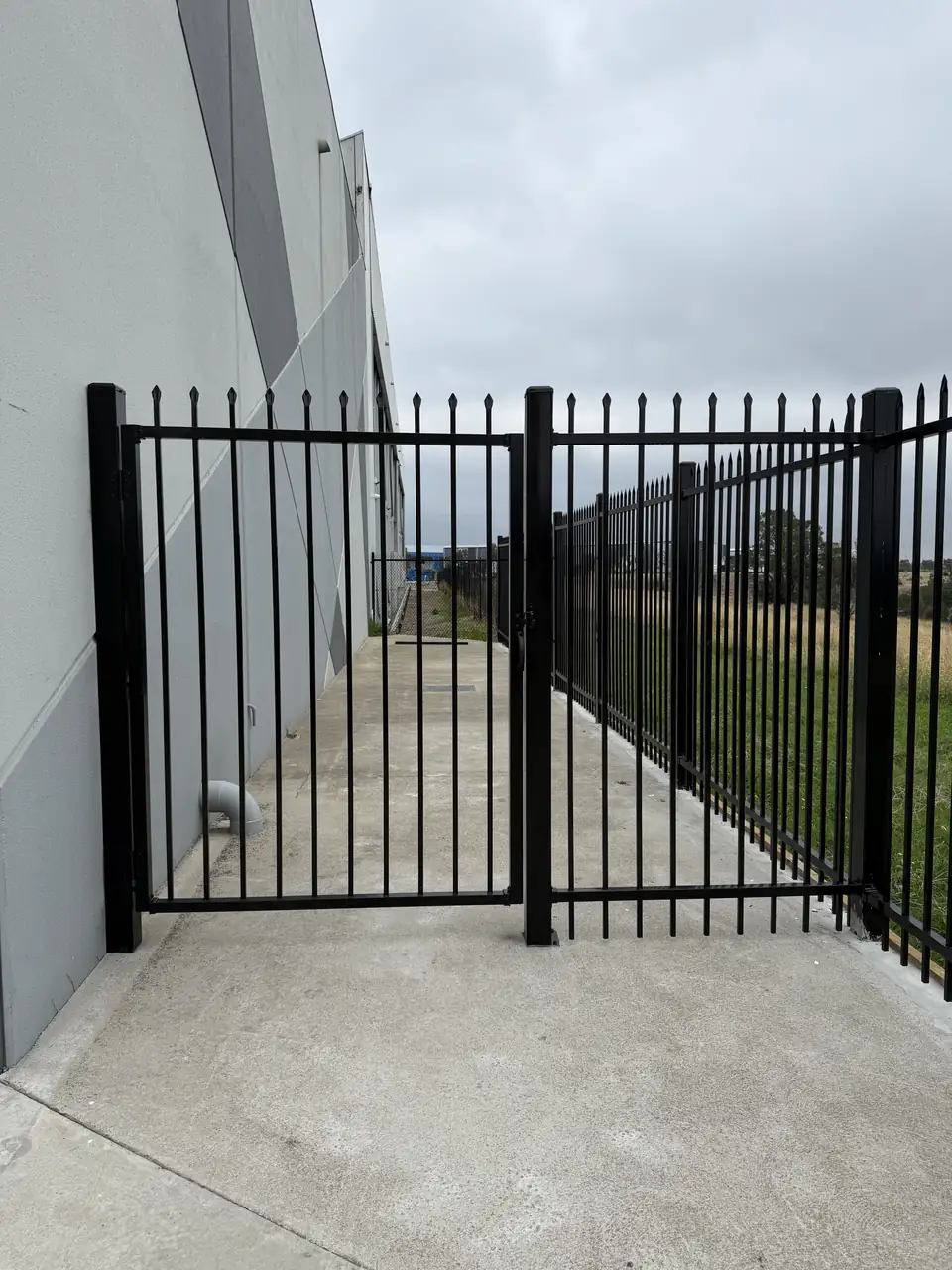 Black steel spear-top gate and fence across a concrete side path beside a building