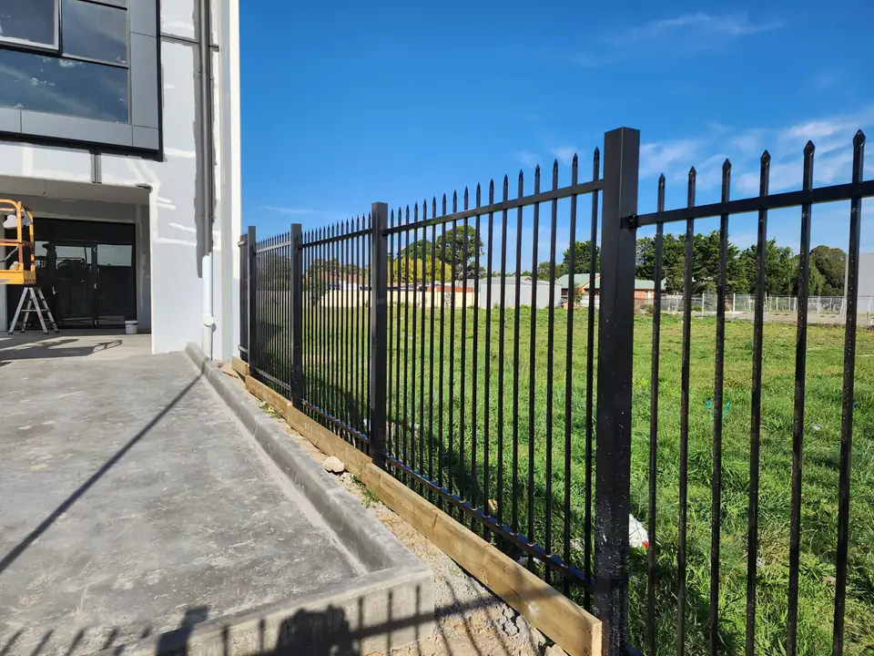 Black steel spear-top fence with a timber board along the bottom, running out from the corner of a new building