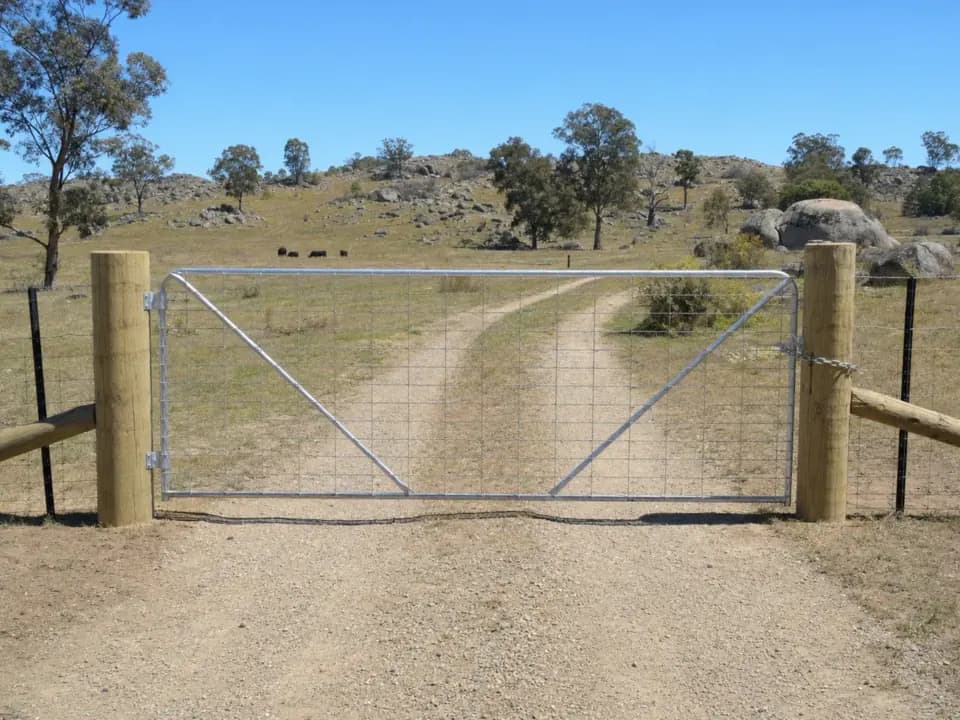 Galvanised steel farm gate hung between pine strainer posts on a farm track in north-east Victoria