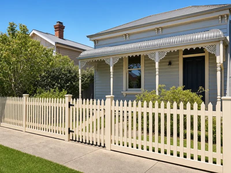 Cream painted timber picket fence and gate in front of a Victorian weatherboard cottage